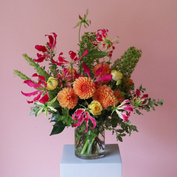 Vase of bight, colourful flowers with dahlias, roses, gloriosa lilies and pineapple lilies.