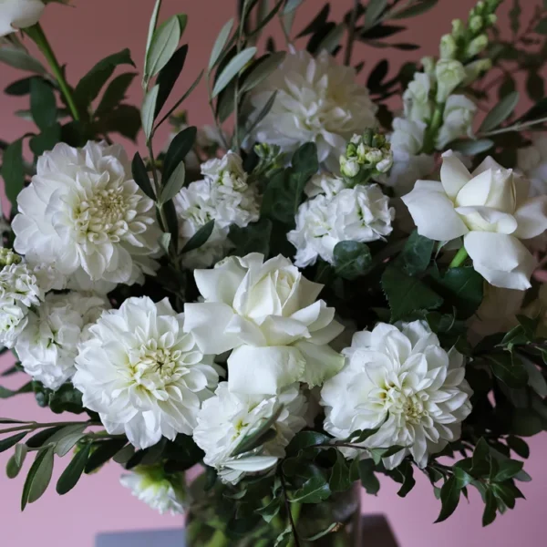 Close up of white flowers including reflexed roses, olive foliage, snap dragons and dahlias.