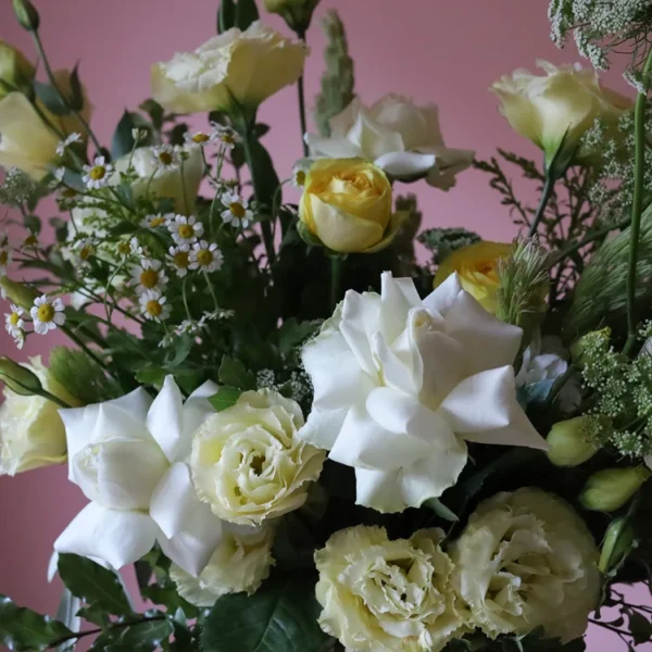 Close up of yellow and white flowers including roses, camomile and lisianthus.