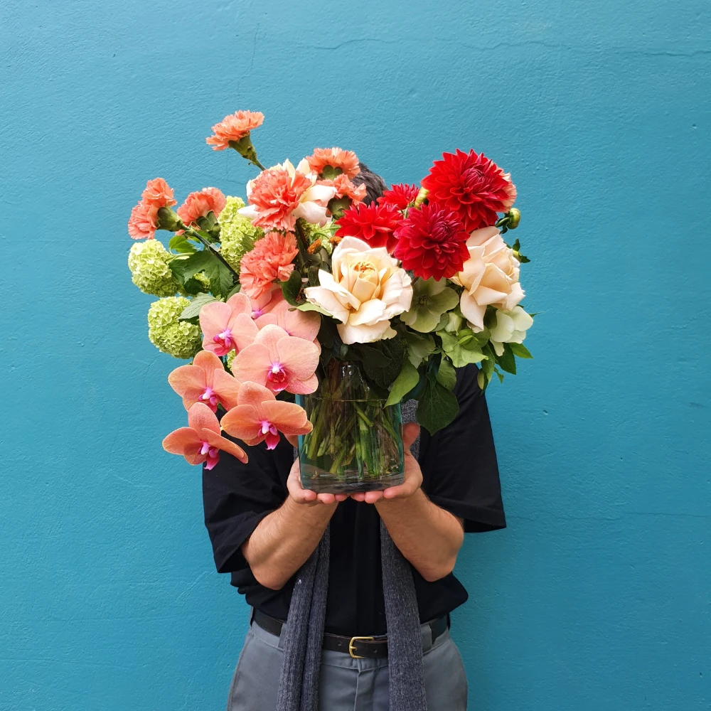 Bright coloured flowers arrangment in a vase feating orchids, roses, snowball and carnations.